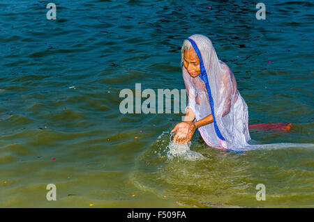 Donna in blu sari in preghiera nell'acqua del fiume Gange mattina presto al sangam, alla confluenza dei fiumi Gange e yamuna Foto Stock