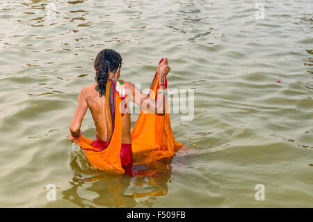 Donna in arancione sari tenendo bagno nell'acqua del fiume Gange mattina presto al sangam, alla confluenza dei fiumi Gange, Foto Stock