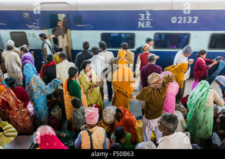 Molte persone in attesa di treni in ritardo su una piattaforma della stazione ferroviaria, spingendo all'interno di un treno in arrivo Foto Stock