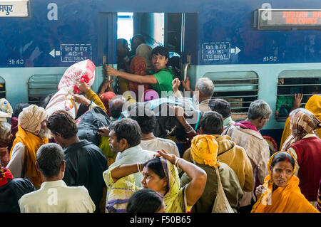 Molte persone in attesa di treni in ritardo su una piattaforma della stazione ferroviaria, spingendo all'interno di un treno in arrivo Foto Stock