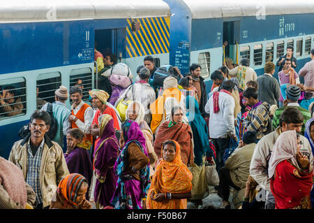 Molte persone in attesa di treni in ritardo su una piattaforma della stazione ferroviaria, spingendo all'interno di un treno in arrivo Foto Stock