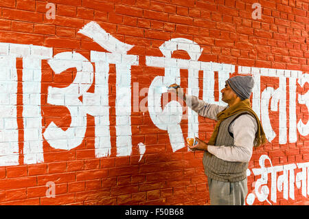 L'uomo bianco pittura lettere in lingua hindi in corrispondenza di una parete rossa Foto Stock