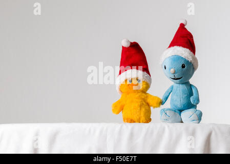 Una luce blu e giallo di un giocattolo di peluche, indossando il babbo natale cappelli, sono seduti insieme su un tavolo bianco Foto Stock