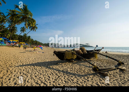 Una vecchia barca da pesca a palolem beach con cielo blu, palme, sabbia bianca e mare blu Foto Stock