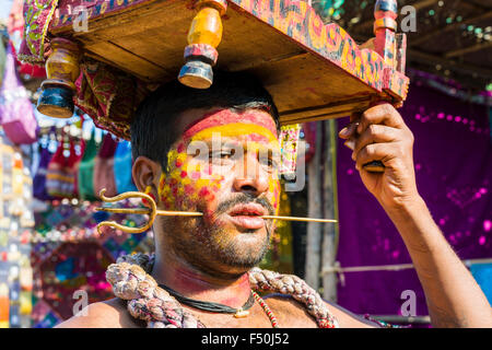Un uomo con un piccolo ottone trident trafitto sua guancia, sta raccogliendo denaro per motivi religiosi al settimanale mercato delle pulci Foto Stock