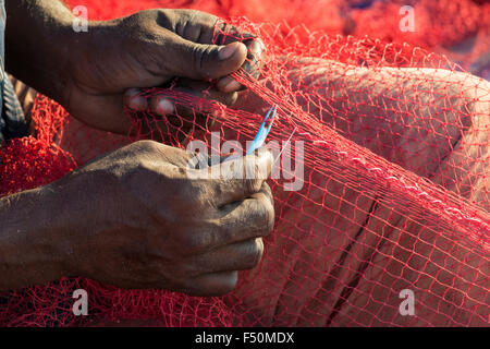 Le mani di un pescatore, chi è la riparazione di rosso le reti da pesca sulla spiaggia Foto Stock