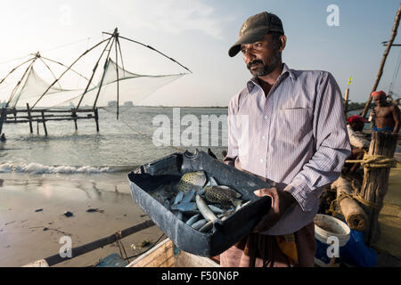 Un uomo è presentare il poco pesce di cattura di un cinese rete da pesca Foto Stock