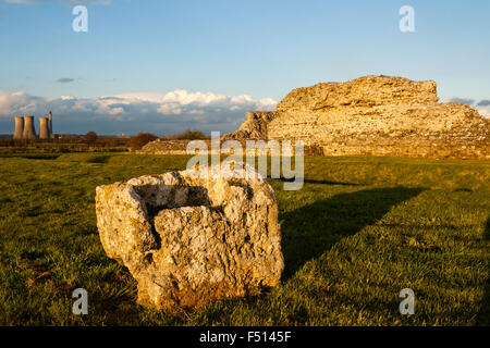 Inghilterra, Richborough castello romano Rutupiae, Saxon Shore fort. Parete ovest e la pietra in primo piano, power station su orizzonte. Ora d'oro, il tramonto. Foto Stock