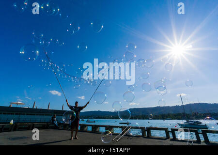 Un uomo è la creazione di un numero elevato di bolle a riva del lago zuerichsee, visto contro la luce del sole Foto Stock