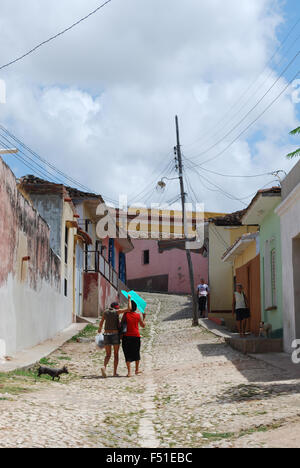 Due signore a piedi lungo una strada a ciottoli stessi ombreggiatura con un ombrello dal sole in Trinidad, Cuba Foto Stock