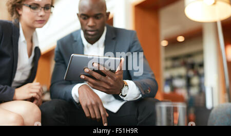 Colpo di imprenditori seduti insieme guardando digitale compressa. Focus sulla tavoletta digitale in mano d'uomo. Foto Stock