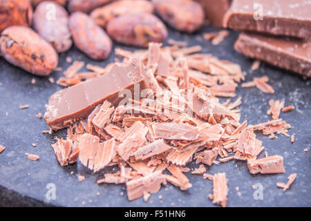 Un mucchio di cioccolato grattugiato, nella parte anteriore delle fave di cacao e di cioccolato al latte Foto Stock