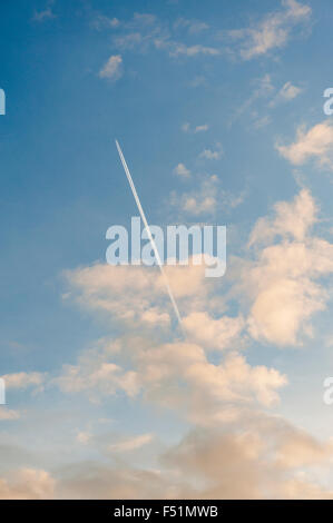 Piano e contrails e nuvole su un cielo blu Foto Stock