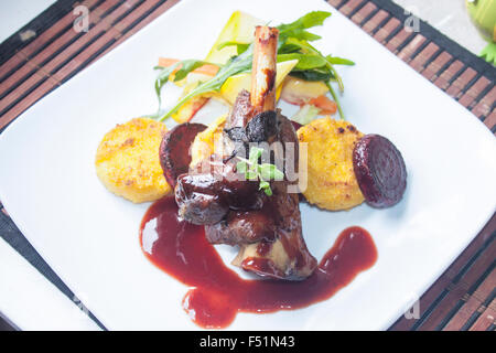 Una piastra piena di gambo di agnello, salsa al vino rosso, polenta, la barbabietola e insalata mista Foto Stock