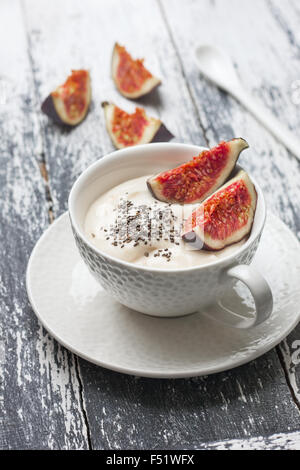 Yogurt con pezzi di fig, chia semi in una tazza di bianco su uno sfondo di legno Foto Stock