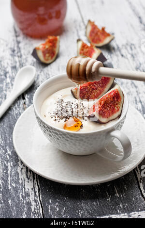 Yogurt con pezzi di fig, chia semi, il miele in un bicchiere di bianco su uno sfondo di legno Foto Stock