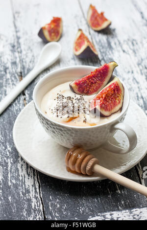 Yogurt con pezzi di fig, chia semi, il miele in un bicchiere di bianco su uno sfondo di legno Foto Stock