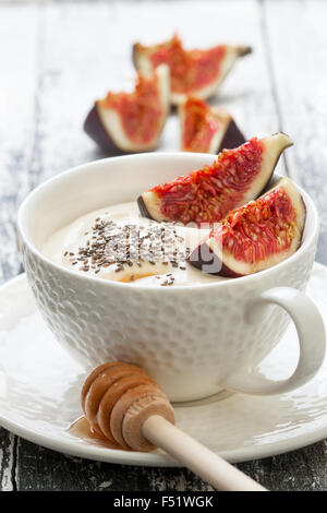 Yogurt con pezzi di fig, chia semi, il miele in un bicchiere di bianco su uno sfondo di legno Foto Stock