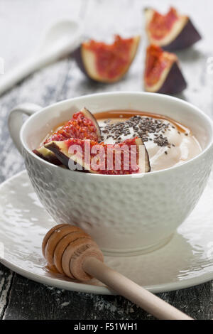 Yogurt con pezzi di fig, chia semi, il miele in un bicchiere di bianco su uno sfondo di legno Foto Stock