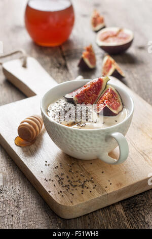 Yogurt con pezzi di fig, chia semi, il miele in un bicchiere di bianco su uno sfondo di legno Foto Stock