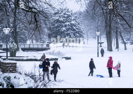 Le persone che si godono la neve invernale in Buxton's Pavilion Gardens, Derbyshire Foto Stock