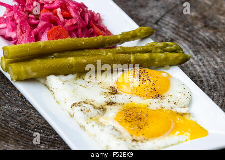 Colazione Leggera consistente in due uova fritte servite con cavolo fermentato e asparagi Foto Stock