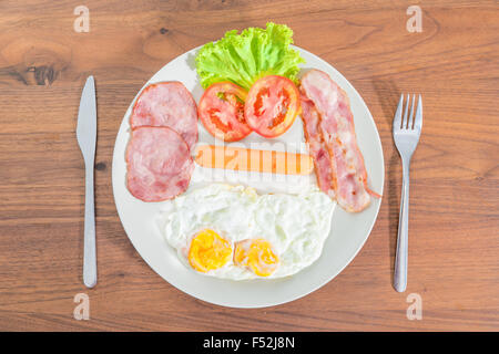 Prima colazione Inglese con uova fritte, pancetta, salsicce, prosciutto e insalata fresca Foto Stock