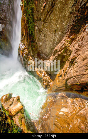 Una potente cascata si tuffa giù da una ripida parete di roccia scura in una turbolenta piscina turchese sottostante. L'acqua crea schiuma bianca e spruzzi quando si schianta contro le rocce umide e robuste del canyon Foto Stock