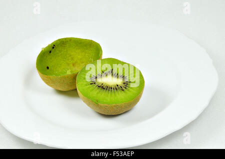 Dimezzato kiwi, pieno e vuoto, sulla piastra bianca con coltello, cucchiaio d'argento, close up, macro, orizzontale, sfondo bianco Foto Stock