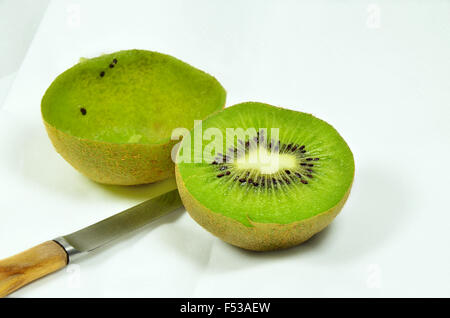 Dimezzato kiwi, pieno e vuoto, sulla piastra bianca con coltello, close up, macro, orizzontale, sfondo bianco Foto Stock