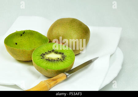 Tre kiwi, dimezzata e complesso, pieno e vuoto, sulla piastra bianca con coltello, close up, macro, orizzontale, sfondo bianco Foto Stock