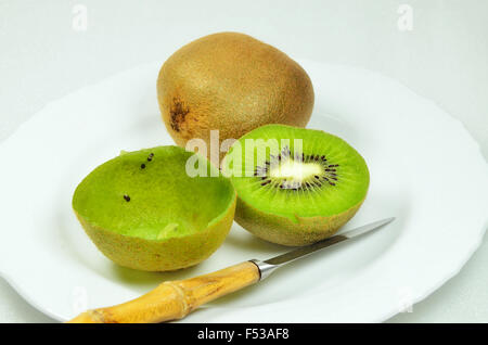 Tre kiwi, dimezzata e complesso, pieno e vuoto, sulla piastra bianca con coltello, close up, macro, orizzontale, sfondo bianco Foto Stock