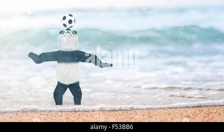 Circo in miniatura panda bambù orsacchiotto sorge sulla spiaggia il Golfo del Siam a sua caviglie in acqua. e a caccia di palla sul naso. soccer p Foto Stock