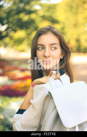 Bella ragazza dello studente con borsa guardò oltre la sua spalla in autunno park. Calda tonalità di colore immagine