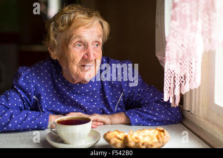 Donna anziana bere il tè seduti ad un tavolo vicino alla finestra. Foto Stock