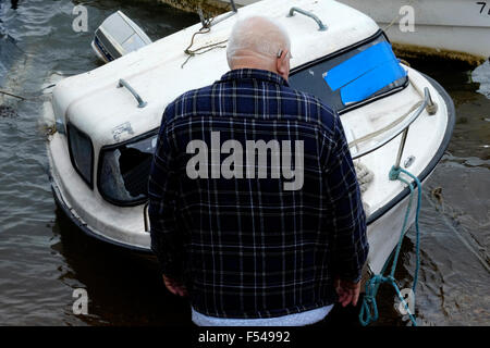 Uomo anziano guardando semi sommerso danneggiato barca nel porto di Portsmouth Inghilterra Regno Unito Foto Stock