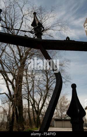 Piegate recinzione in ferro post con alberi e cielo in background. Foto Stock