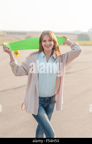 Giovane ragazza in piedi con uno skateboard in strada. Foto Stock