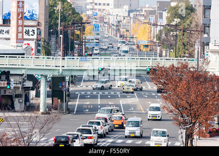 Giappone, Wakayama. Vista lungo cinque lane city street con metallo verde ponte pedonale che attraversano. Occupato con il traffico, teleobiettivo con vista. Foto Stock