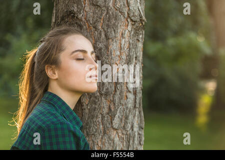 Bella donna con gli occhi chiusi appoggiato sul tronco di albero in posizione di parcheggio Foto Stock