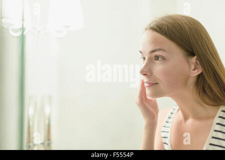 Bella donna di applicare la crema sulla faccia in bagno interno Foto Stock