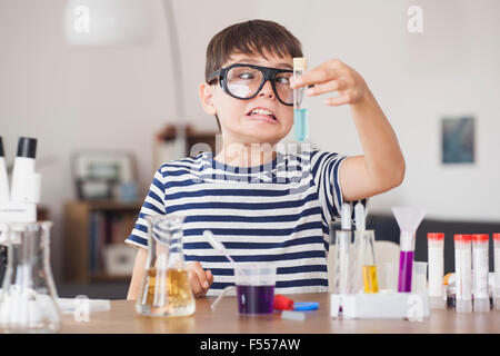 Cross eyed boy guardando al tubo di prova durante la scienza esperimento in casa Foto Stock