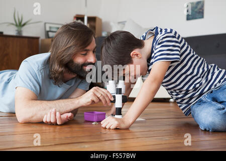 Padre e figlio mediante microscopio su pavimento in legno duro Foto Stock