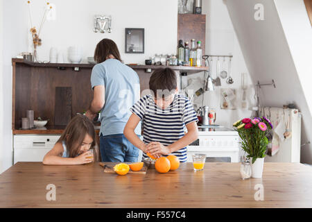 Ragazzo la spremitura di arance mentre suor bere il succo con padre in background in cucina Foto Stock