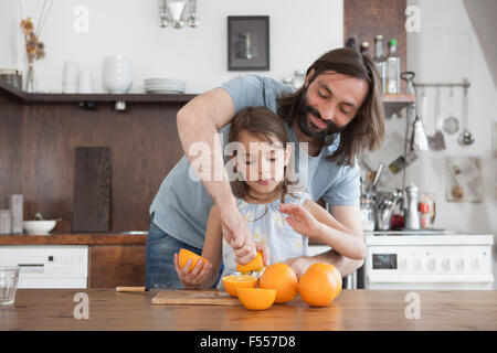 Padre ad assistere la figlia spremute di arancia in cucina Foto Stock