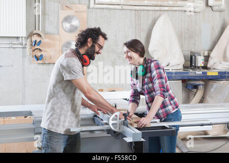 Vista laterale di ridere i colleghi utilizzando una tavola scorrevole visto in officina Foto Stock