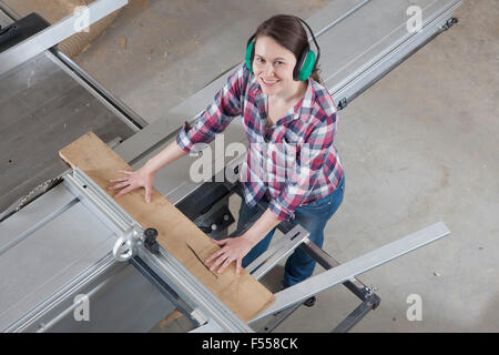 Angolo alto ritratto di felice falegname femmina utilizzando una tavola scorrevole visto in officina Foto Stock