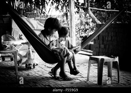 Due ragazzi guardare uno smart phone mentre è seduto in una amaca in loro di proprietà di una famiglia fabbrica di mattoni nel Delta del Mekong, Vietnam del Sud. Foto Stock