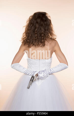 Vista posteriore della sposa azienda pistola contro sfondo colorato Foto Stock