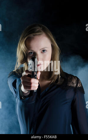 Giovane donna puntando una pistola al buio Foto Stock